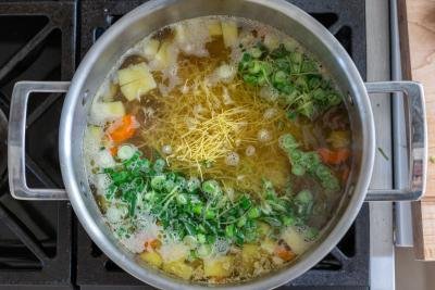 A pot with cooking chicken noodle soup