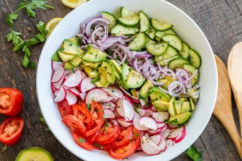 Salad in a bowl, tomatoes, radishes, avocado, onion and cucumber with dressing on top