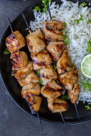Chicken skewers on a plate with rice and herbs.