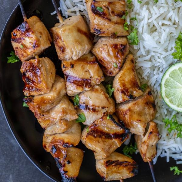 Chicken skewers on a plate with rice and herbs.