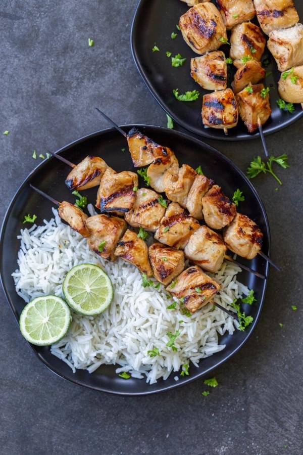 Chicken skewers on a plate with rice and herbs.