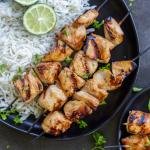 Chicken skewers on a plate with rice and herbs.