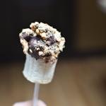 A half of a banana on a lollipop stick dipped into chocolate and walnuts