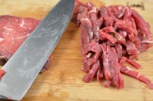 Beef being sliced into thin slices on a cutting board