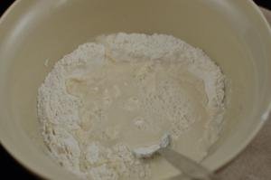 Water, yeast and flour being combined in a bowl with spoon