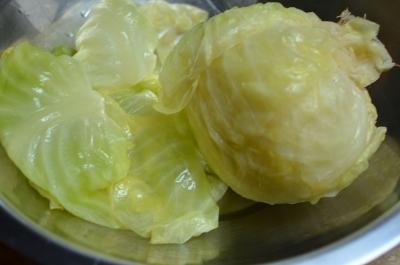 A full cabbage head in a bowl with the leaves being taken off the head