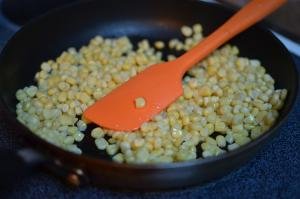 Corn being fried on a frying pan and mixed using a spatula