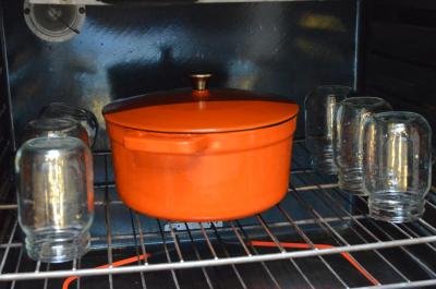An oven filled with jars that are inside down and a ceramic pot with the stewed meat