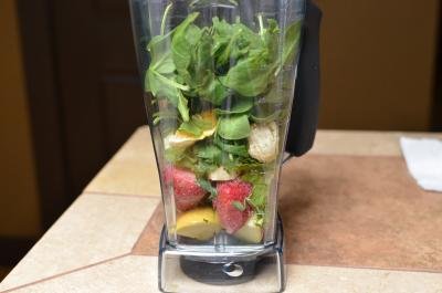 Strawberries, bananas, kale, apples, orange and spinach in a blender on a table top