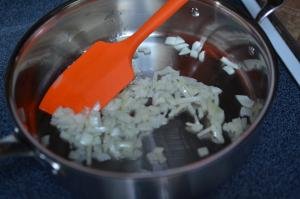 Onions being sautéed in a saucepan and mixed using a spatula