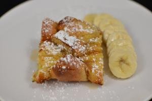 Baked French Toast sprinkled with powdered sugar and banana slices besides it on a plate