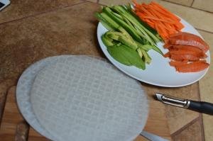 A plate with long thin strips of salmon, carrots, cucumbers, and avocado and rice paper next to the plate