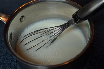Milk in a pot on the stove top with a whisk in the pot