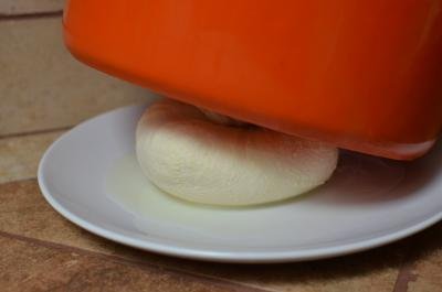 Cheese wrapped tightly in cheesecloth and placed on a plate with a heavy pot standing on top of it