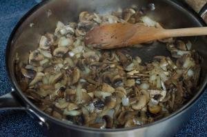 Mushrooms and onions being fried in a skillet with white wine