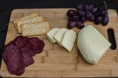 A cheese board with meats, crackers, homemade cheese and grapes