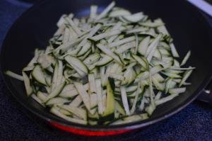 Zucchini cut into long thin strips on a skillet on a stove top