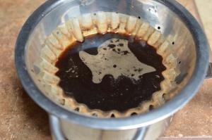 Coffee filter placed over a strainer, and having the coffee and water mixture run through it