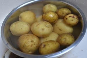 Unpeeled potatoes getting rinsed in a bowl
