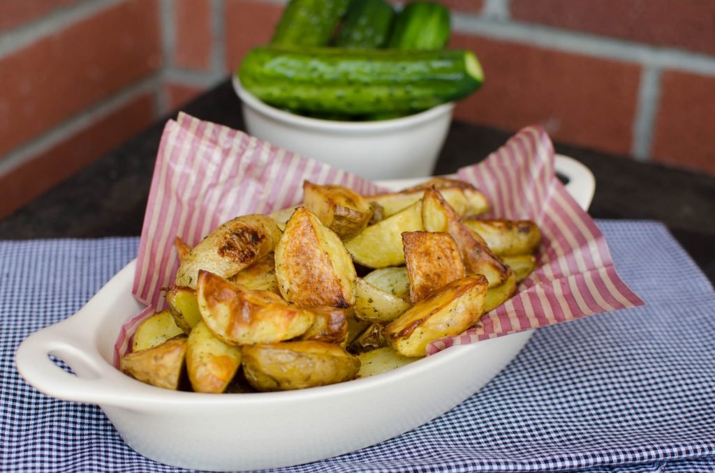 Ranch roasted potatoes in a serving bowl on a table with cucumbers in the background