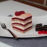 A slice of raspberry vanilla cream cake on a plate with a fork and chocolate squares next to it