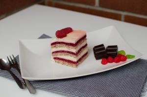 A slice of raspberry vanilla cream cake on a plate with a fork and chocolate squares next to it