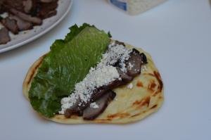 Lamb meat sliced up on top of naan bread with feta on top and lettuce
