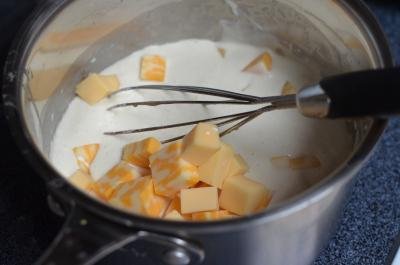 Butter, milk, cheese, whipping cream, flour, and dijon mustard in a saucepan being whisked together