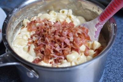 Macaroni and cheese in a pot with bacon being added into it