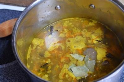 Bay leaves and seasoning added to a pot of soup on the stove top