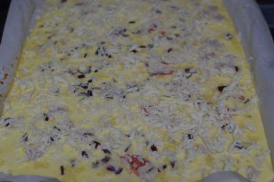 Omelette Roll mixture poured over a baking pan that is lined with parchment paper and sprinkled with cheese