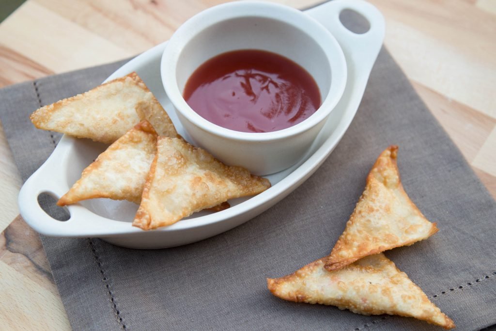 Crunchy puffs in a plate with a little bowl of sweet and sour sauce all on a table