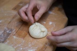 A round piroshki having the sides pinched together on a floured cutting board