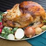 Turkey on a serving tray surrounded with veggies like brussels, onions, potatoes, radishes, onions and carrots