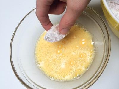 Chicken bites covered in cornstarch mixture being dipped into whisked eggs