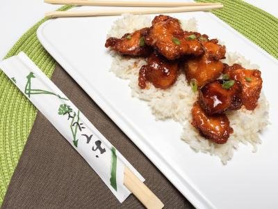Sweet and Sour Chicken on rice on a plate with chopsticks besides the plate