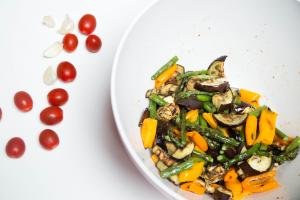 Roasted Vegetables in a bowl with fresh tomatoes and garlic next to the bowl