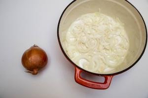 Onions sliced into half rings and placed into the bottom of a baking pot and a fresh onion next to the pot