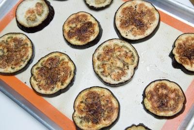 Cooked eggplant slices laid out on a baking sheet lined with a silicon mat with oil and salt sprinkled on top of them