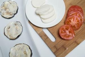 Eggplant slices with garlic mayo on them and a cutting board with tomato and mozzarella slices