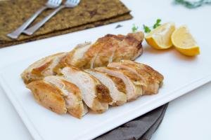 Beer Roasted Chicken cut up into slices layer out in rows on a plate with lemon slices