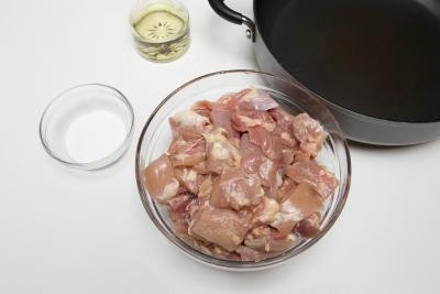 Chicken in a bowl cut into 2 inch pieces, a bowl of salt and oil next to a skillet