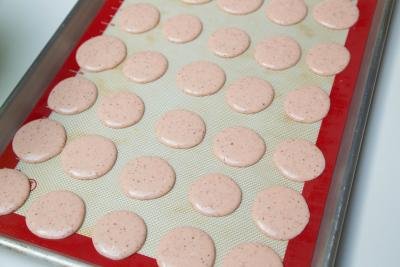 Pink macarons pipped onto a baking sheet lined with a silicon mat