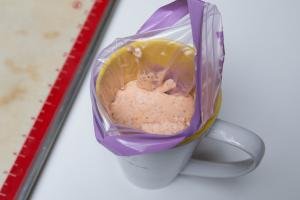 A ziploc bag corner placed into a cup and being filled with the macaron batter