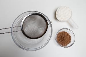 A bowl with a strainer on top and cocoa and flour besides the bowl