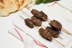 Beef Kofte Kebab on a plate with green onions, cucumbers and naan bread above the plate