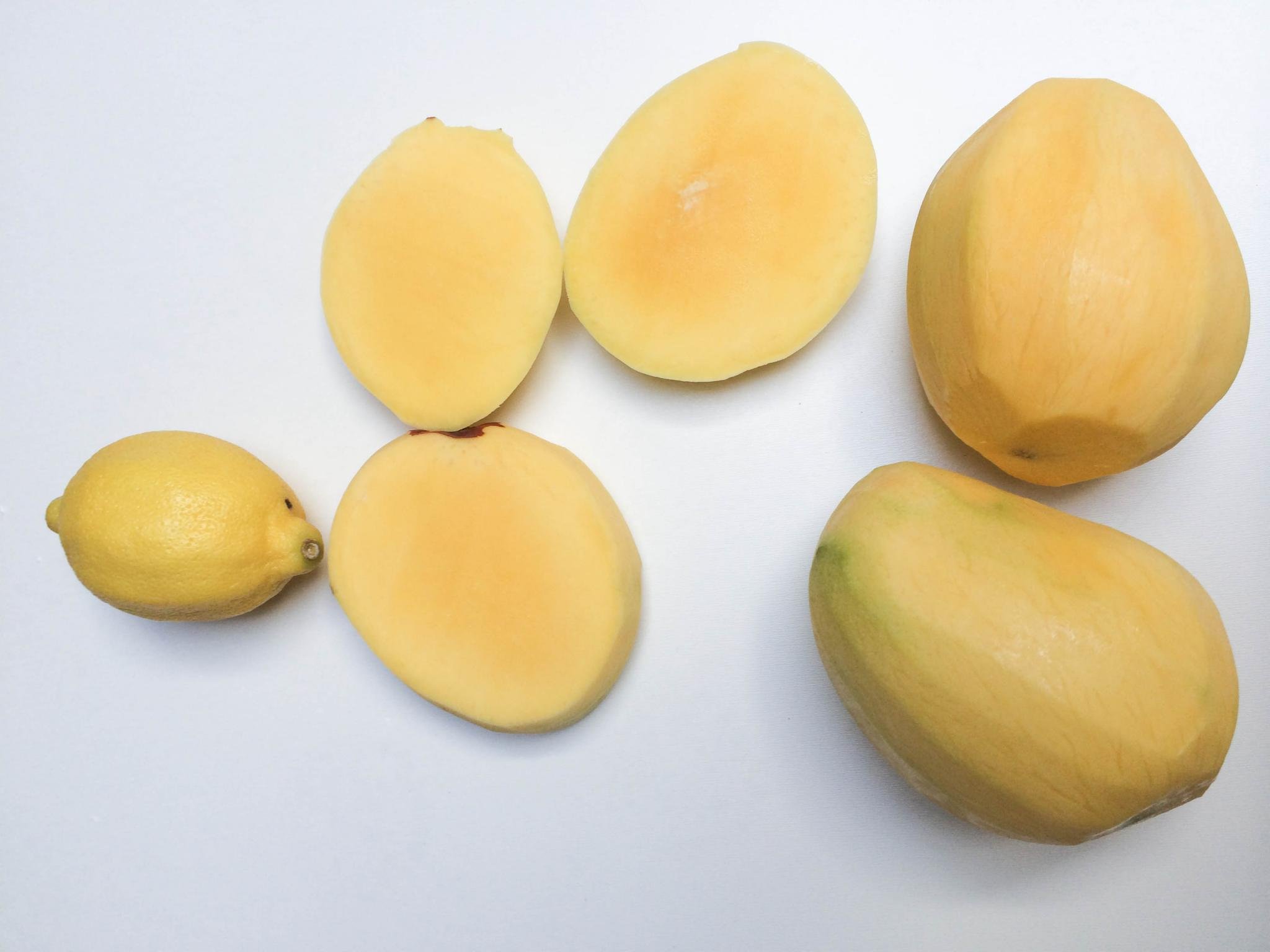 <b>Mangos</b> peeled and 2 of them are cut in half and a lemon besides the <b>mangos</b>.