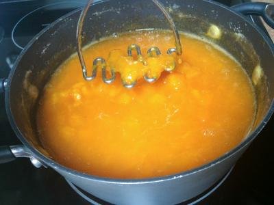 Apricots in the pot with sugar being mashed with a potato masher