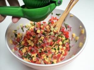A lime being squeezed into a bowl with the salsa mixture