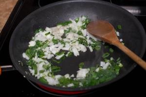 Yellow and green onion being sautéed in a skillet